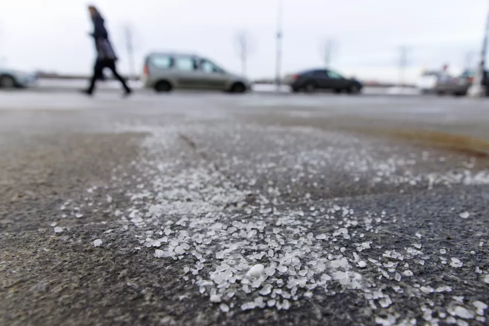 Low close-up of salt sprinkled on asphalt road in winter with person walking and car in background.